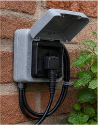 Prise extérieure étanche à clapet sur un mur de briques, câble branché qui forme une boucle vers le bas