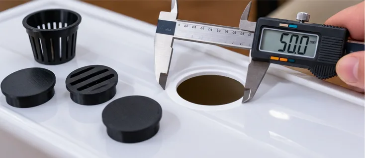 Pied à coulisse mesurant un trou de 50 mm dans une gouttière, avec un panier et des bouchons imprimés à côté