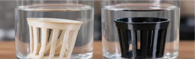 Deux paniers imprimés plongés dans des verres d’eau : le blanc en PLA déformé, le noir en PETG intact