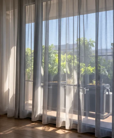 Voilage tiré devant une baie vitrée, potager à l’ombre derrière